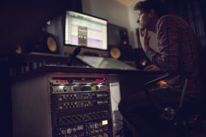 Audio rack and sound recording equipment in recording studio with sound engineer working in the background.